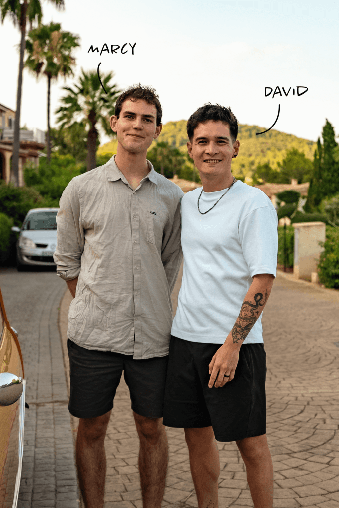 Marcel und David stehen lächelnd vor einem Hintergrund mit Palmen